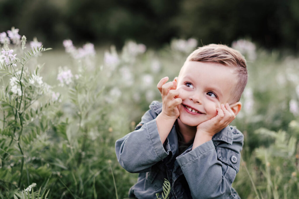 Familienfotograf Leipzig. Kleiner Junge sitzt im Gras und lächelt.